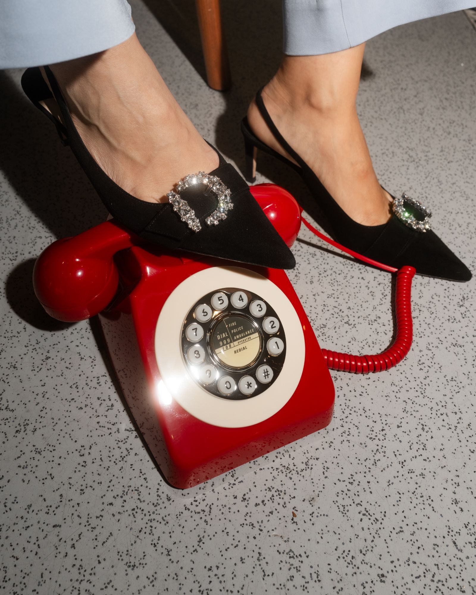 Black heels resting on a red vintage telephone